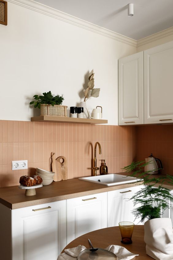 a chic warm kitchen with white cabinetry, butcherblock countertops, a terracotta tile backsplash