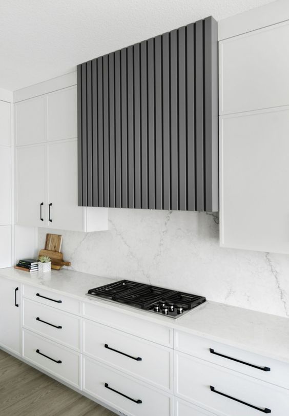 a chic white kitchen with a grey fluted hood, a white stone backsplash and countertops is a chic and cool space