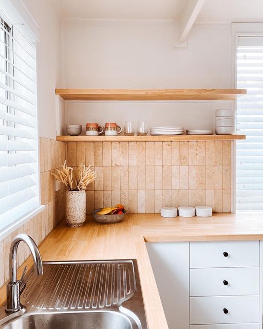 a chic white kitchen with butcherblock countertops, a skinny terracotta tile backsplash and open shelves