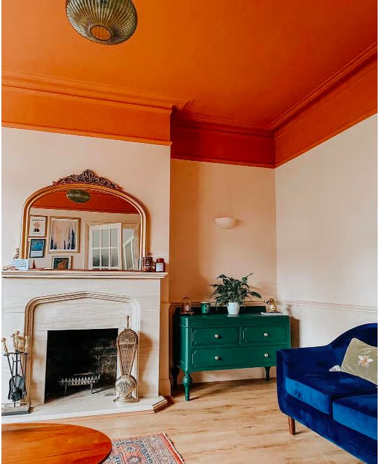 A color infused living room with an orange ceiling, a fireplace, a navy sofa and a green bureau, a rug and a coffee table