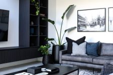 a contemporary living room with a dark TV unit, grey sofas, a black coffee table, pillows and potted greenery