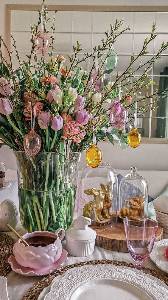 a cool Easter centerpiece of greenery branches, pink and white tulips and roses and plastic sheer eggs hanging on the branches