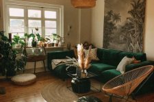 a cool boho living room with a bold green sectional, a coffee table, a round chair, potted plants, some art and pampas grass
