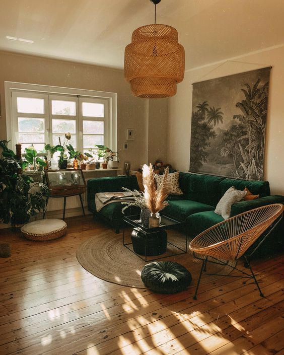 a cool boho living room with a bold green sectional, a coffee table, a round chair, potted plants, some art and pampas grass