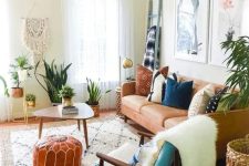 a cozy boho living room with a tan leather couch, a blue chair, a coffee table, potted greenery, a macrame piece and artworks