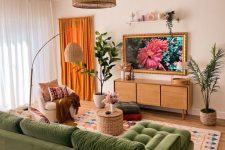 a cozy living room with a green sectiona, a rug, a curved sofa, a side table, a TV unit, a woven chandelier and potted plants