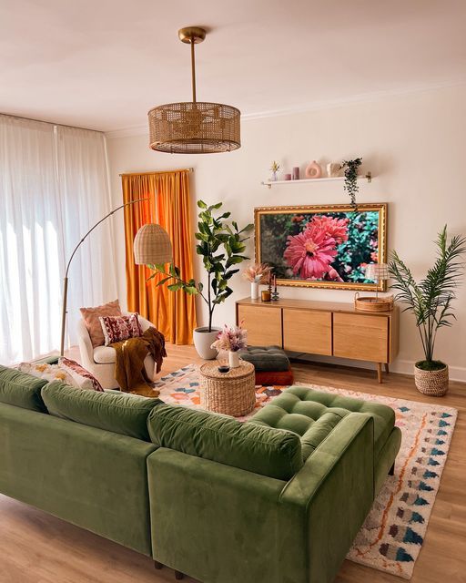 a cozy living room with a green sectiona, a rug, a curved sofa, a side table, a TV unit, a woven chandelier and potted plants