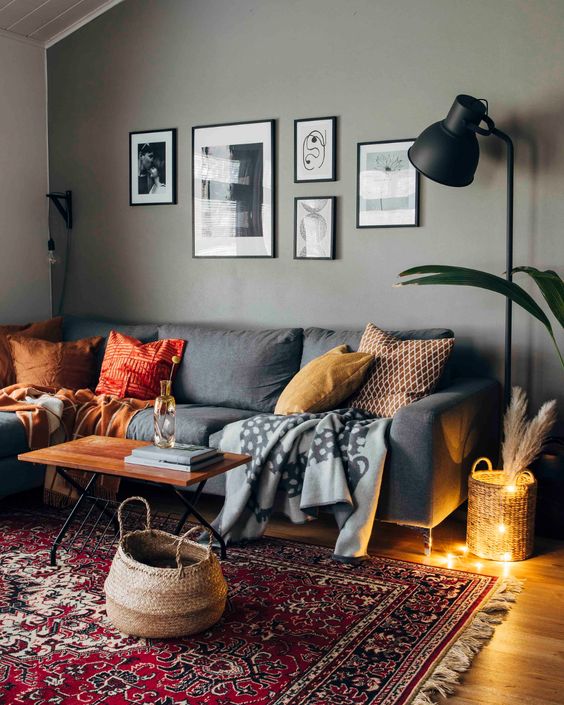 a cozy modern living room with a grey accent wall, a grey sofa with pillows, a black lamp, a gallery wall and a printed rug