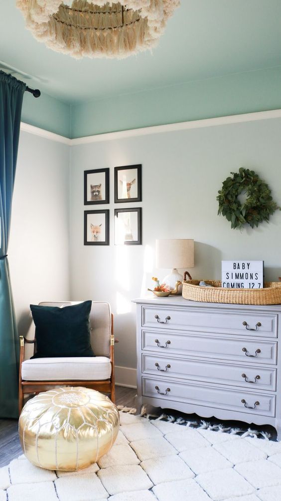 a cozy nursery with pale green walls and an aqua ceiling, a grey dresser, a rattan chair and a fringe chandelier