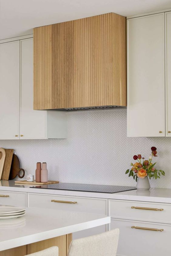 a creamy kitchen with a herringbone backsplash, white countertops, a fluted hood and gold handles