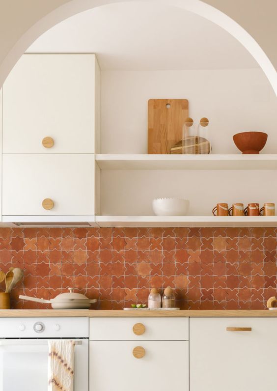 a creamy kitchen with sleek cabinets, butcherblock countertops, a bold terracotta tile backsplash and open shelves