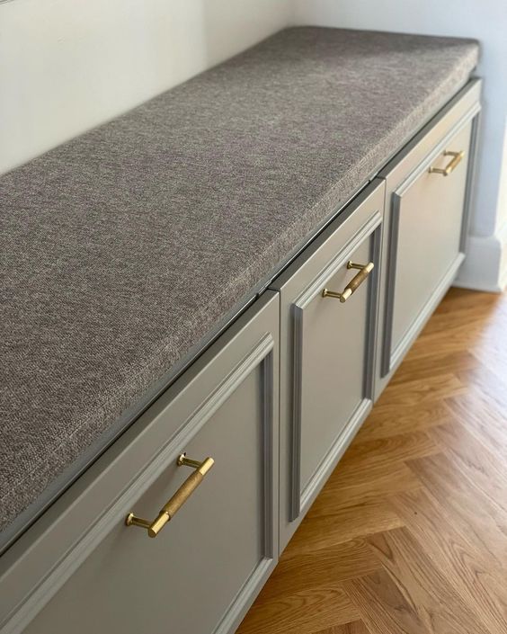 a grey storage bench built of IKEA Metod, with shaker cabinets, gold handles and a grey seat on top is stylish