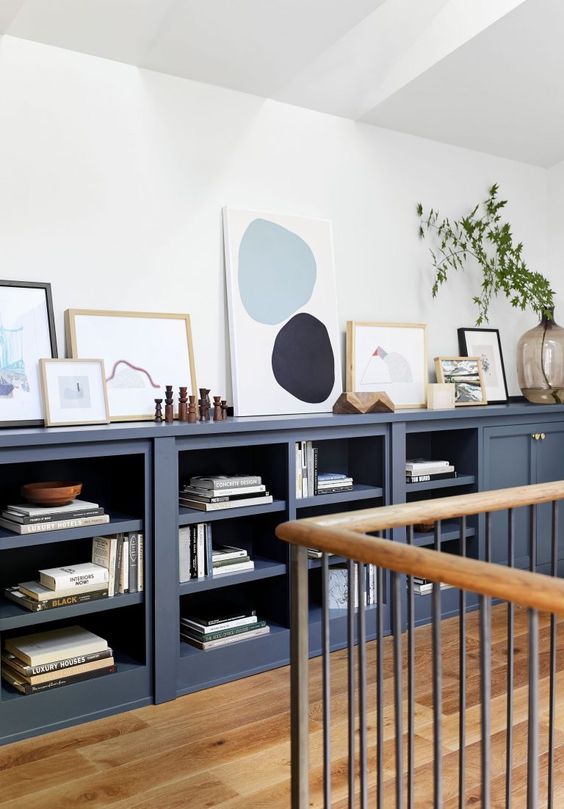a large navy sideboard with open and closed storage compartments, with books, decor, artwork and greenery is amazing