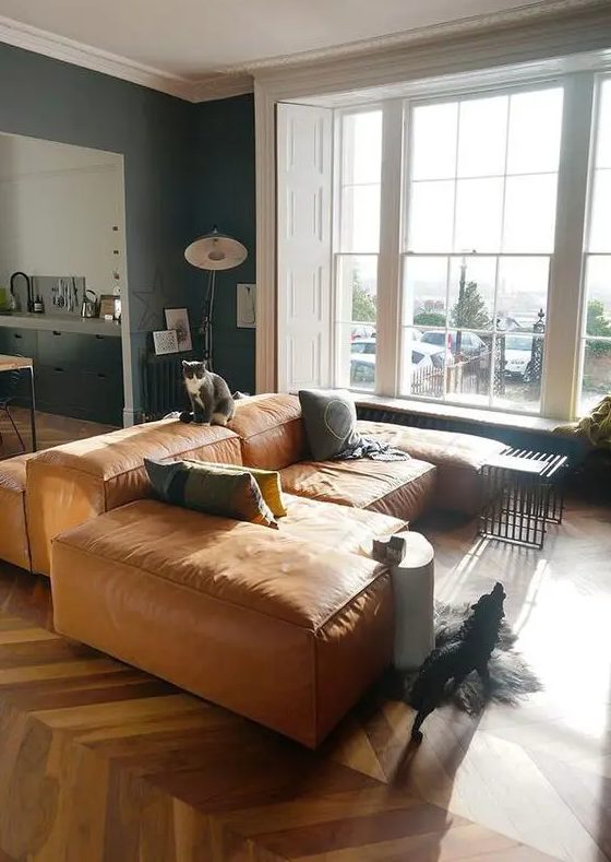 A light filled living room with an oversized tan leather low sofa, printed pillows and some lamps and decor