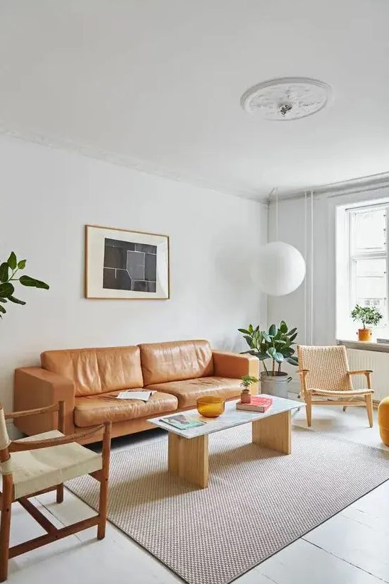 a light-filled mid-century modern living room with an amber leather sofa, neutral chairs and a simple coffee table, a pendant lamp