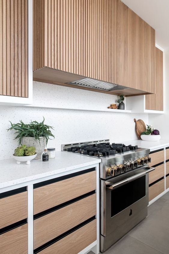 a light-stained kitchen with white terrazzo countertops and a backsplash plus a fluted hood and some ledges