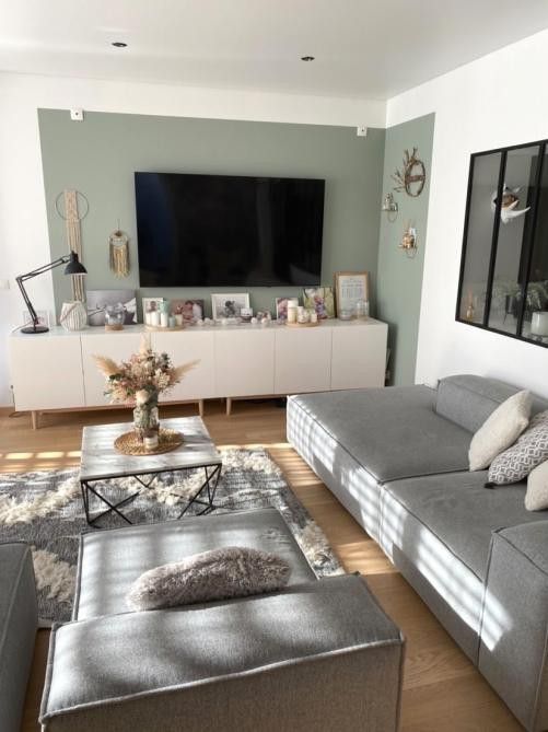 a lovely Scandi living room with a green accent wall, a low grey sofa and a grey rug, boho decor and candles