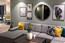 a lovely living room with a grey accent wall, a grey sectional sofa, a coffee table, a gallery wall and yellow accents