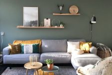 a lovely modern living room with a dark green wall, a grey sofa with pillows, shelves with decor, coffee tables and a chair