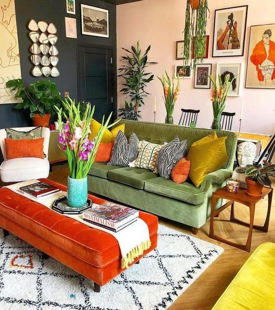 a maximalist living room with graphite grey and blush walls, a green sofa, an orange ottoman, colorful pillows and potted plants