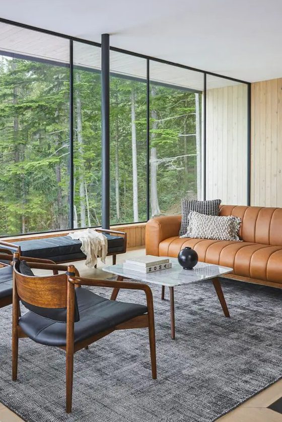 A mid century modern livign room with a tan leather couch, a black daybed and chairs, a coffee table and printed chairs