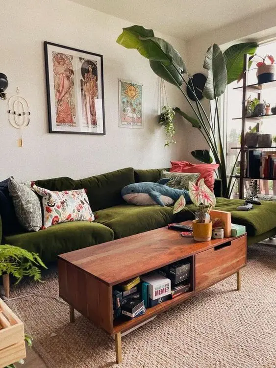 a mid-century modern living room with a green sectional, a coffee table, statement plants, decor and a shelving unit