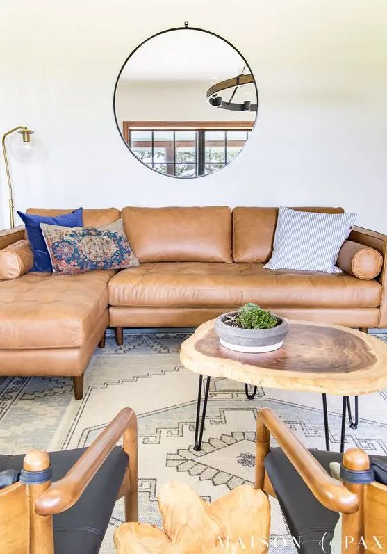 a mid-century modern living room with a tan leather sectional, black chairs, a living edge coffee table and a printed rug