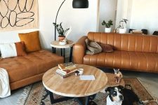 a mid-century modern space with a tan leather sofa and an ottoman, a printed rug, a coffee table, a black floor lamp and some art