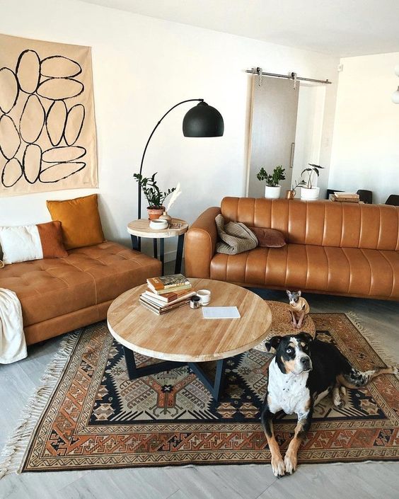 A mid century modern space with a tan leather sofa and an ottoman, a printed rug, a coffee table, a black floor lamp and some art
