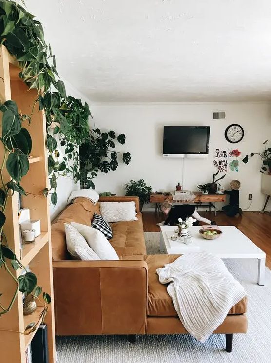 A mid century modern to boho living room with a tan leather sectional, a large coffee table, a bench and lots of potted greenery