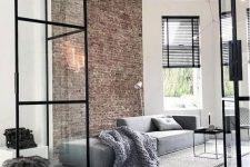 a minimalist living room with a brick wall, a grey sofa, a black coffee table and black shades