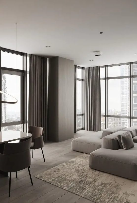A minimalist taupe living room with floor to ceiling windows, a greige low sofa, taupe curtains and a pretty tan rug