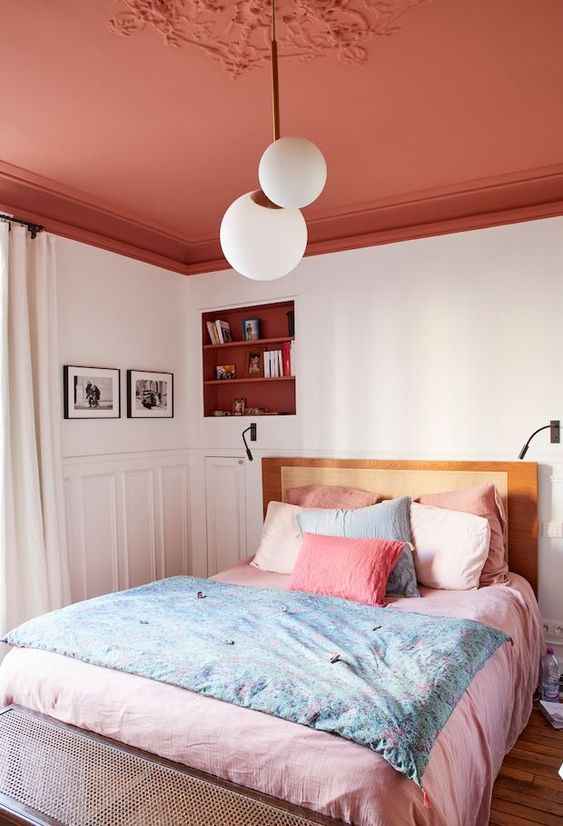 a modern bedroom with a red ceiling, a niche with shelves, a bed with pink bedding and some art and lamps