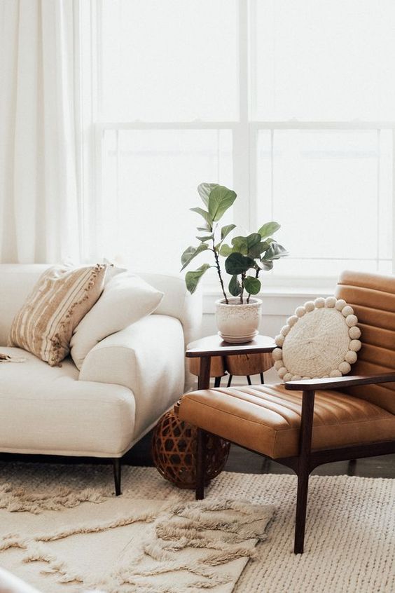 a modern boho living room with layered boho rugs, a creamy sofa, a leather chair, some boho decor