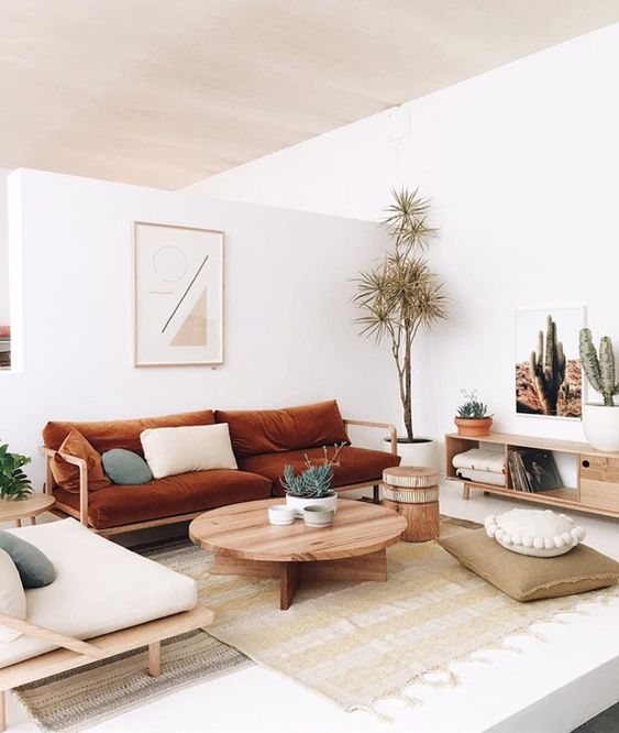 a modern boho living room with layered rugs, a rust sofa and a neutral chair, a coffee table and a credenza, some potted plants