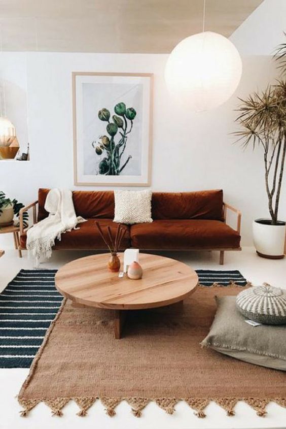 a modern boho living room with layered rugs, a rust sofa, pillows, a coffee table and some plants and decor