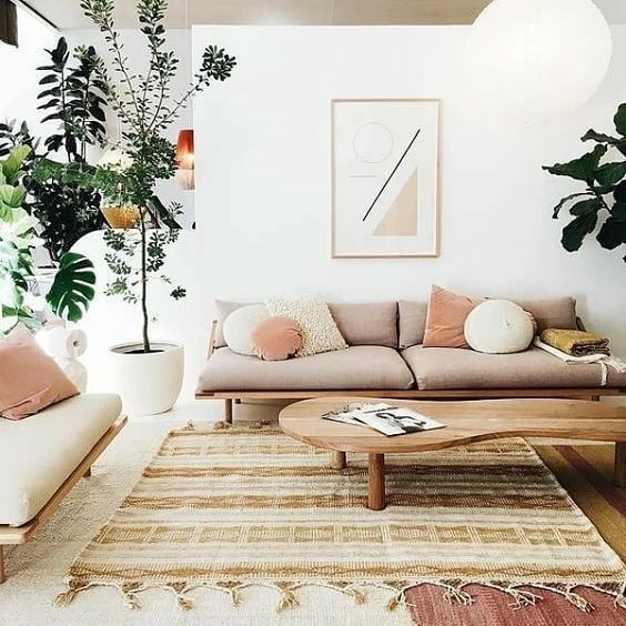 a modern earthy living room with layered rugs, seating furniture with pillows, a table and potted plants