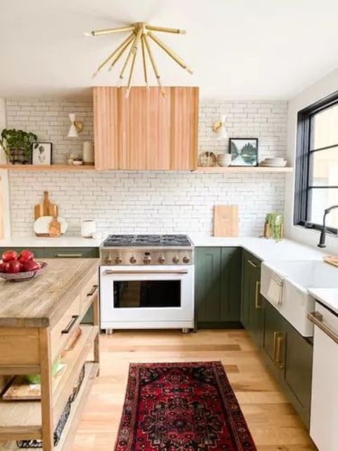 a modern farmhouse kitchen with green cabinets, a brick wall, a fluted hood and shelves, a wooden kitchen island