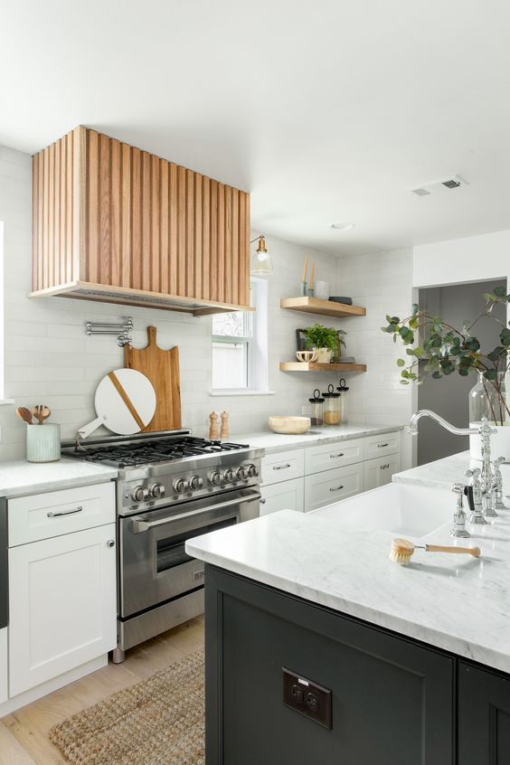 a modern farmhouse kitchen with white cabinets and a black kitchen island, white countertops, a fluted hood and open shelves