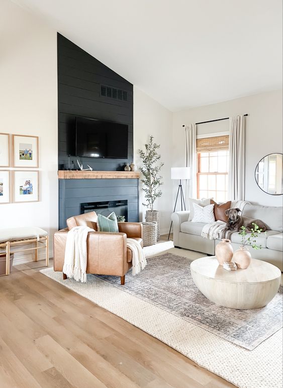 a modern farmhouse living room with a fireplace, a grey sofa, an amber chair, layered rugs, a gallery wall and some decor