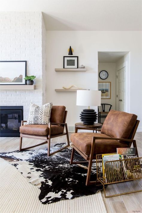 a modern farmhouse living room with a fireplac,e brown leather chairs, layered rugs, shelves with decor and a magazine stand