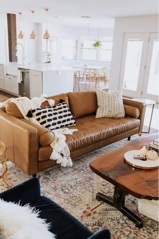 a modern farmhouse living room with a tan leather couch and a navy velvet one, a living edge table and printed rugs is wow