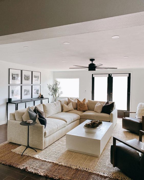 a modern farmhouse living room with layered rugs, a neutral sofa, a coffee table, brown chairs, a gallery wall and a black console