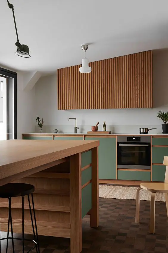 a modern kitchen with green cabinets, a fluted hood, a large kitchen island with green touches and some chairs