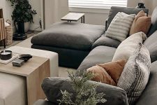 a modern living room with a graphite grey sofa and pillows, a side tables, an ottoman and some lovely decor and plants