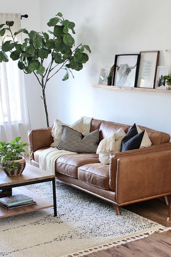 a modern living room with a tan leather sofa, a tiered coffee table, a ledge gallery wall, a rug and potted plants