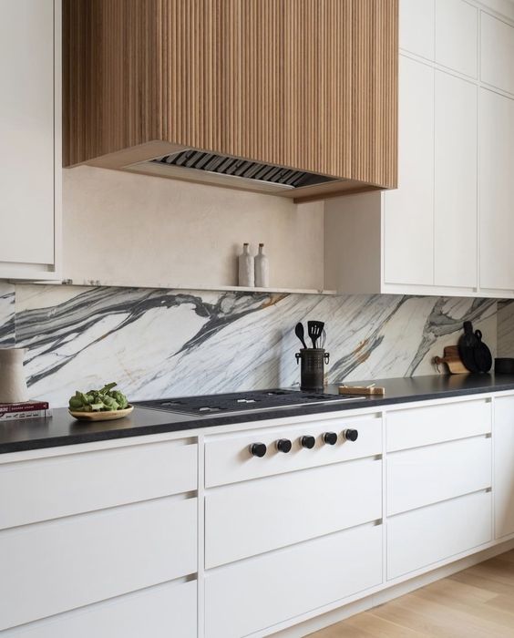 a modern neutral kitchen with black countertops, a stone backsplash, a fluted hood is a chic and refined space