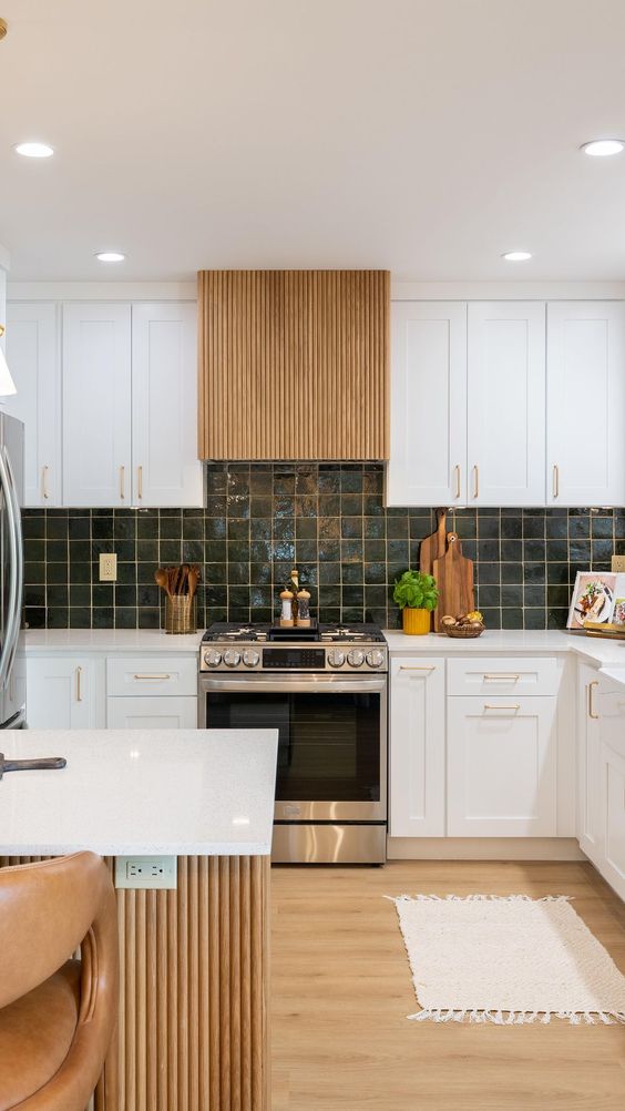 a modern white kitchen with a dark green tile backsplash, white countertops, a fluted hood and a kitchen island