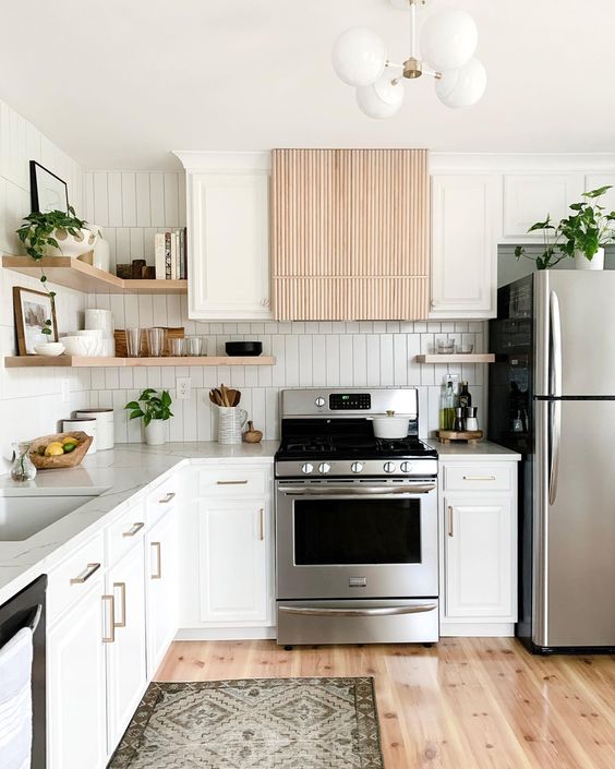 a modern white kitchen with a stacked tile backsplash, a fluted hood and stainless steel appliances and open shelves