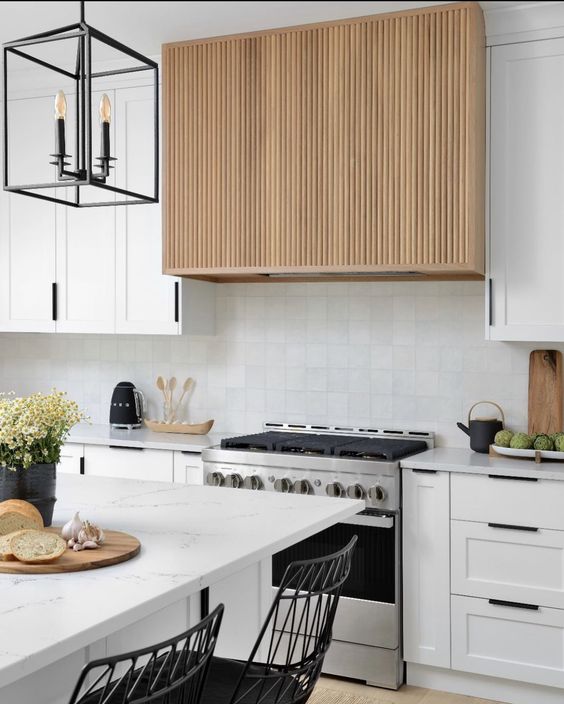 a modern white kitchen with a white tile backsplash, a fluted hood, a neutral kitchen island, a black lamp and stools
